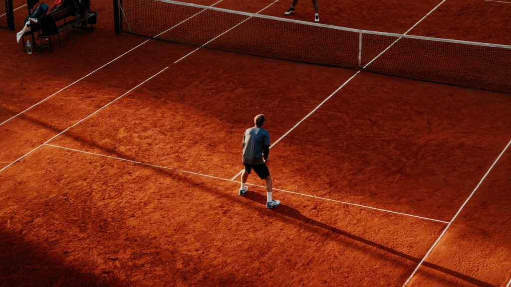 Tennis players competing on a sunlit red clay court in Buenos Aires.