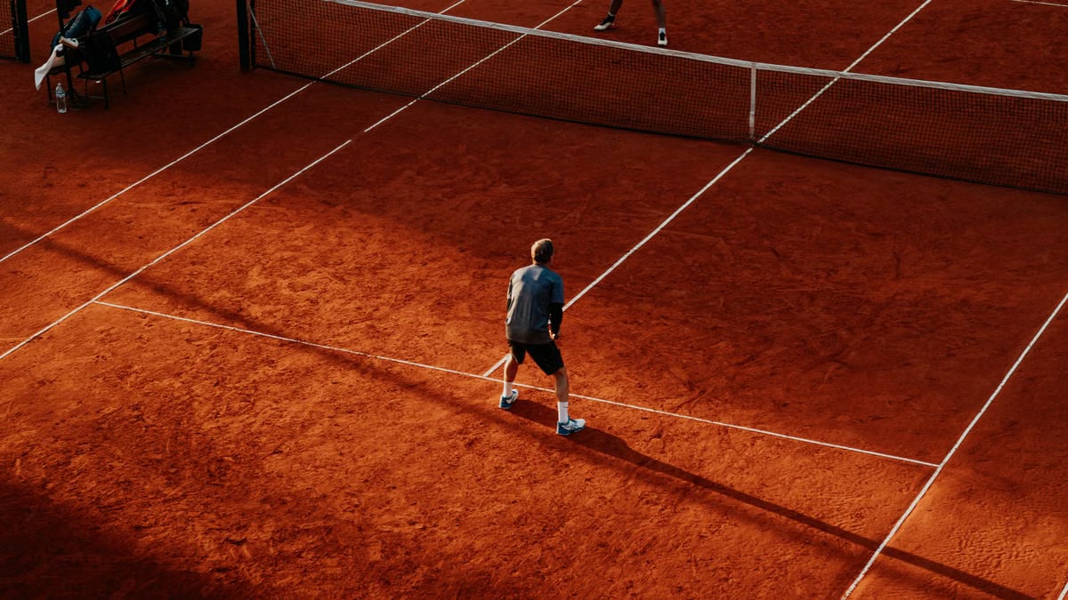 Tennis players competing on a sunlit red clay court in Buenos Aires.