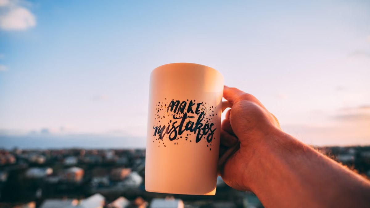 A hand holding a motivational mug with 'Make Mistakes' against a sunset in Lviv.